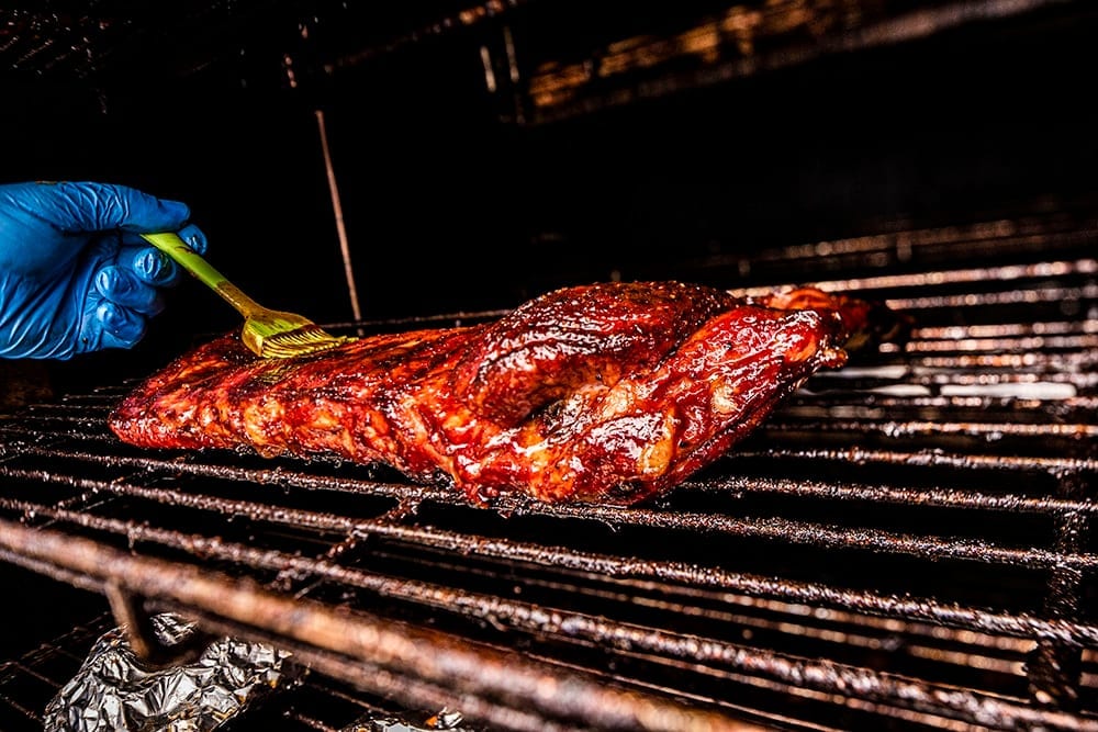 A Carson City BBQ pitmaster tending racks of ribs on the on-site rotisserie smoker