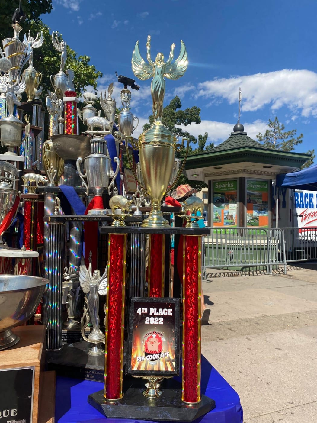 Tall flame-topped trophies standing on a draped table at an outdoor cook-off, one plaque reading "4th Place 2022".