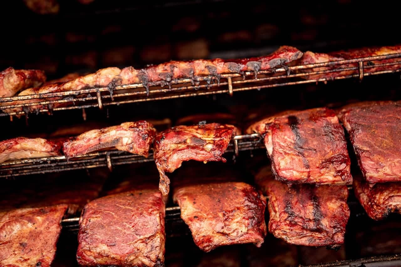 Tiers of rib racks packed onto the shelves of a commercial smoker, seen from the open door.