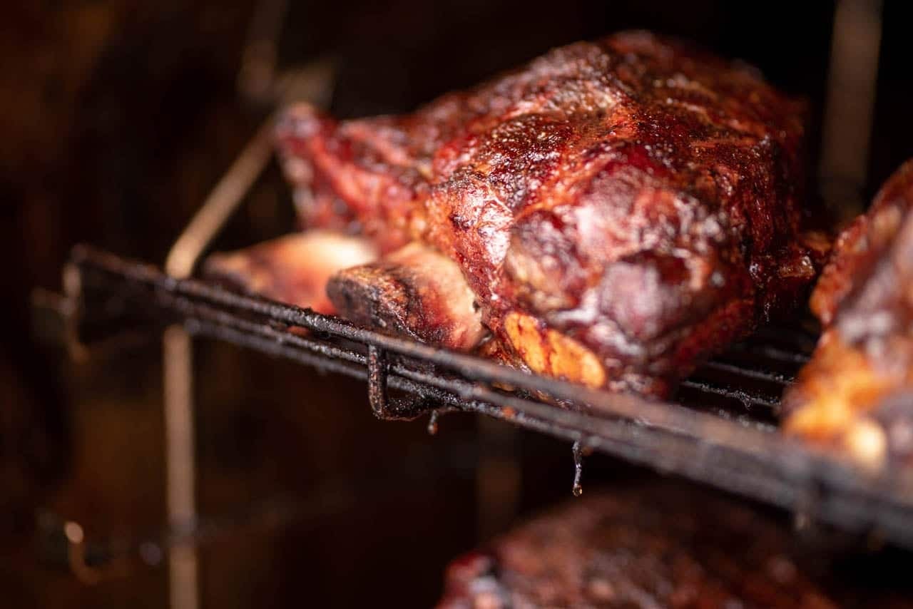 A whole cut of dark, glazed smoked meat resting on a rotisserie rack inside the cooker.