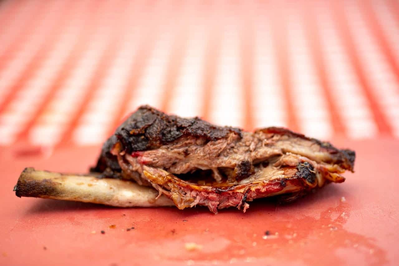 A close-up of a single meaty rib bone with a heavy bark crust, resting on a red cutting board.