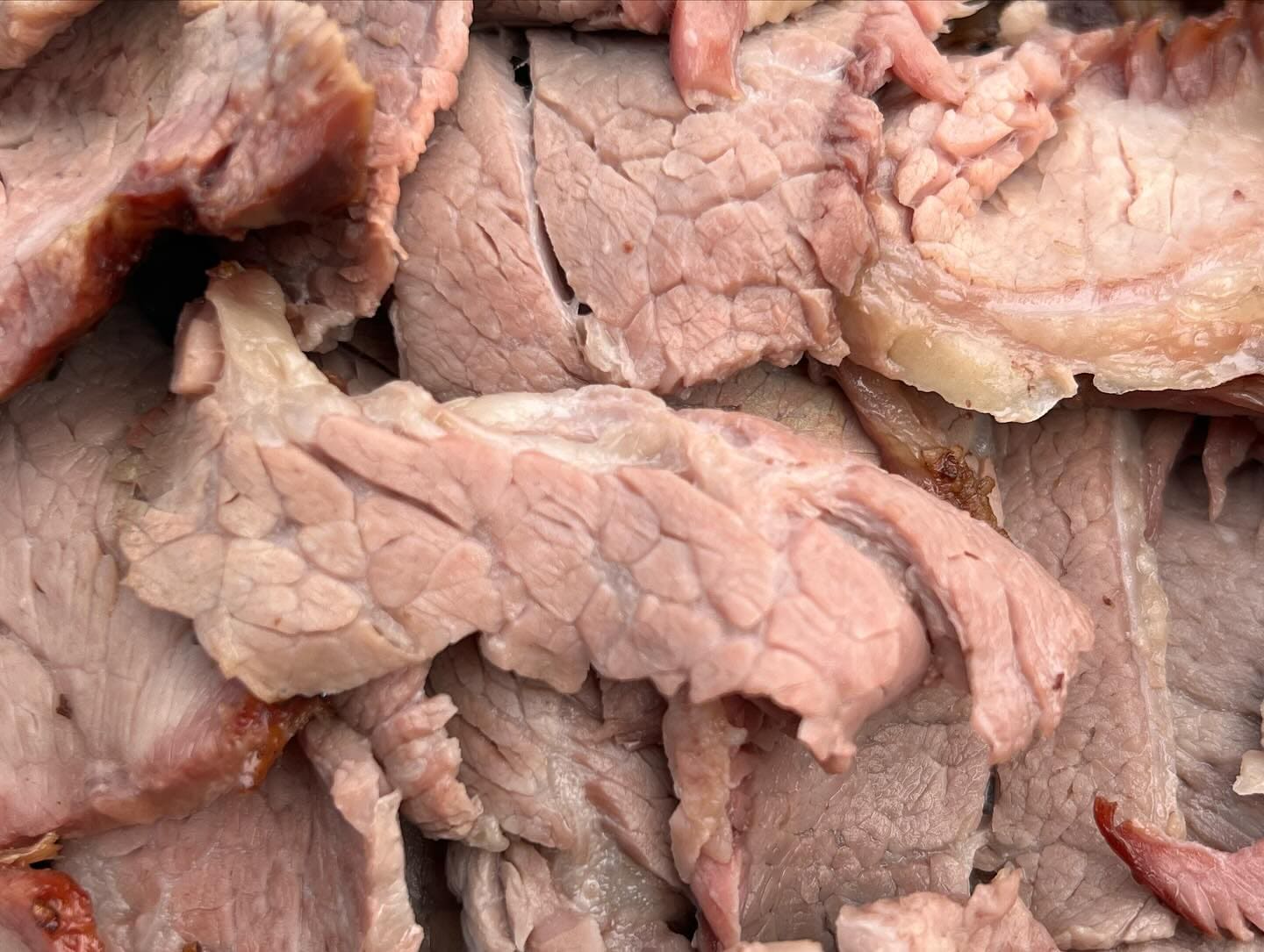 A close-up of thick-sliced smoked tri-tip, pink through the centre and piled in a serving tray.