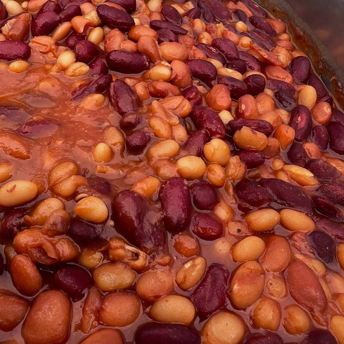 A close-up of BBQ baked beans, a mix of kidney and white beans in a thick red sauce.