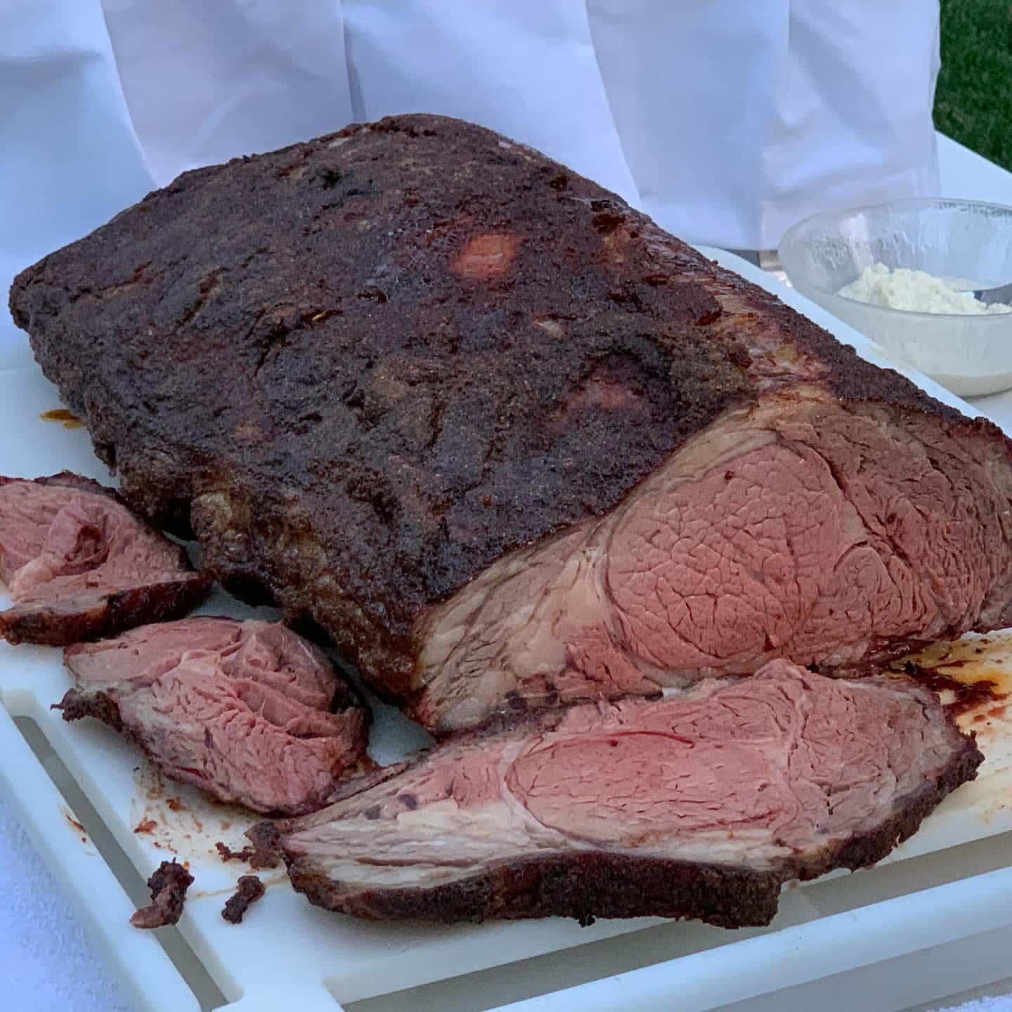 A whole peppered prime rib on a serving platter, partly carved to show the rare pink interior against its dark crust.