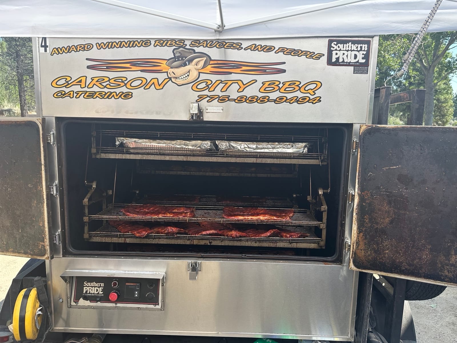 The Carson City BBQ Southern Pride rotisserie trailer with its doors open, racks of meat visible inside