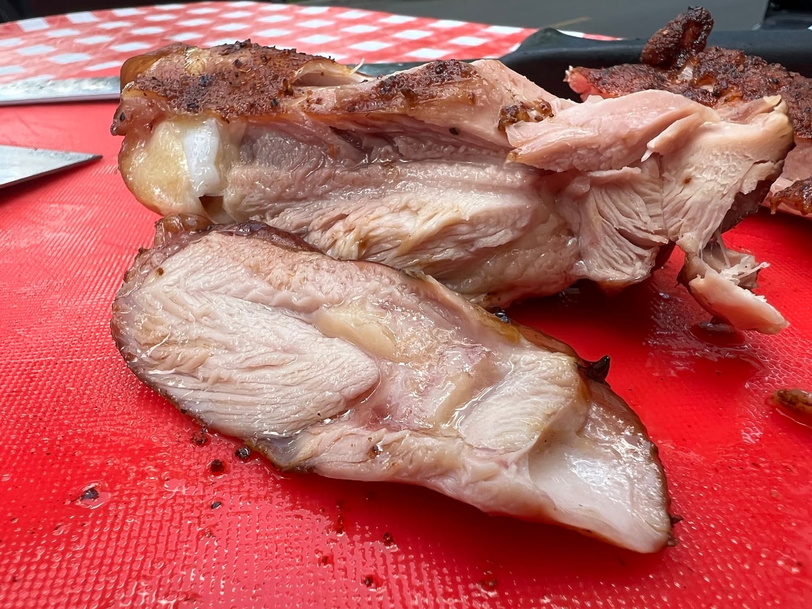 Pulled and sliced smoked chicken on a red cutting board, the meat pale and visibly juicy.