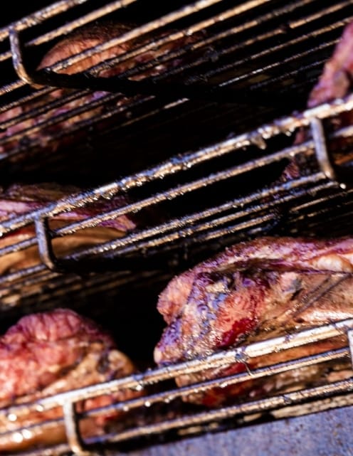 Large cuts of beef resting across the wire racks inside a dark smoker cabinet.