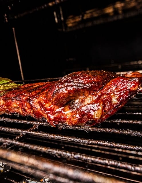 A sauced rack of ribs glowing red-brown on the grill bars inside the cooker.