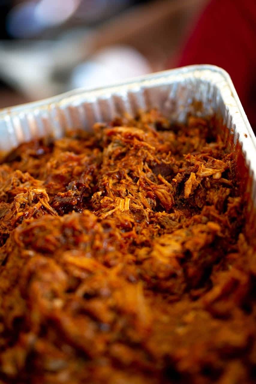 A full foil tray of shredded pulled pork, glistening and tossed in sauce.