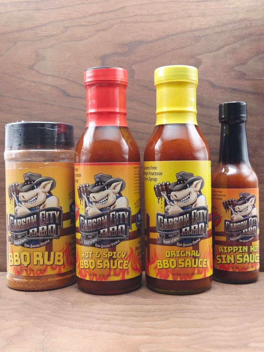 The Carson City BBQ sauce bottles and rub shaker lined up on a dark wood surface
